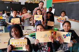 کلاسی از بچه‌ها دفترچه‌های سپاسگزاری دست ساز خود را که کلماتی مانند «آزادی»، «عشق» و «برادر» را نشان می‌دهد، در دست دارند.
